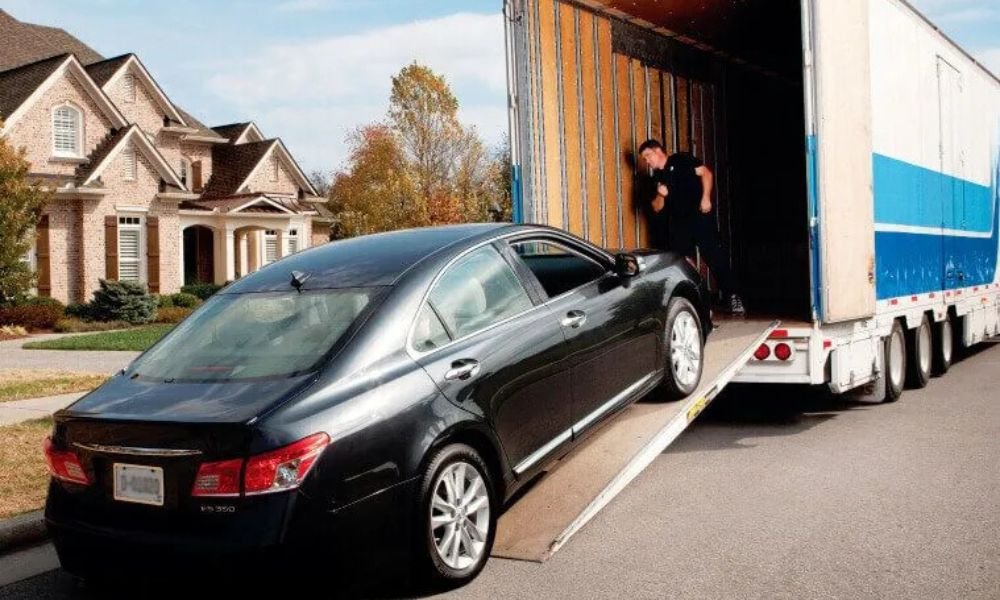 a black car loading in an enclosed car truck and a men stand inside the truck